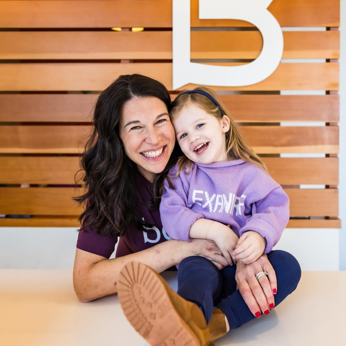 Studio owner Lindsay McConnell with her young daughter at the studio front desk, smiling